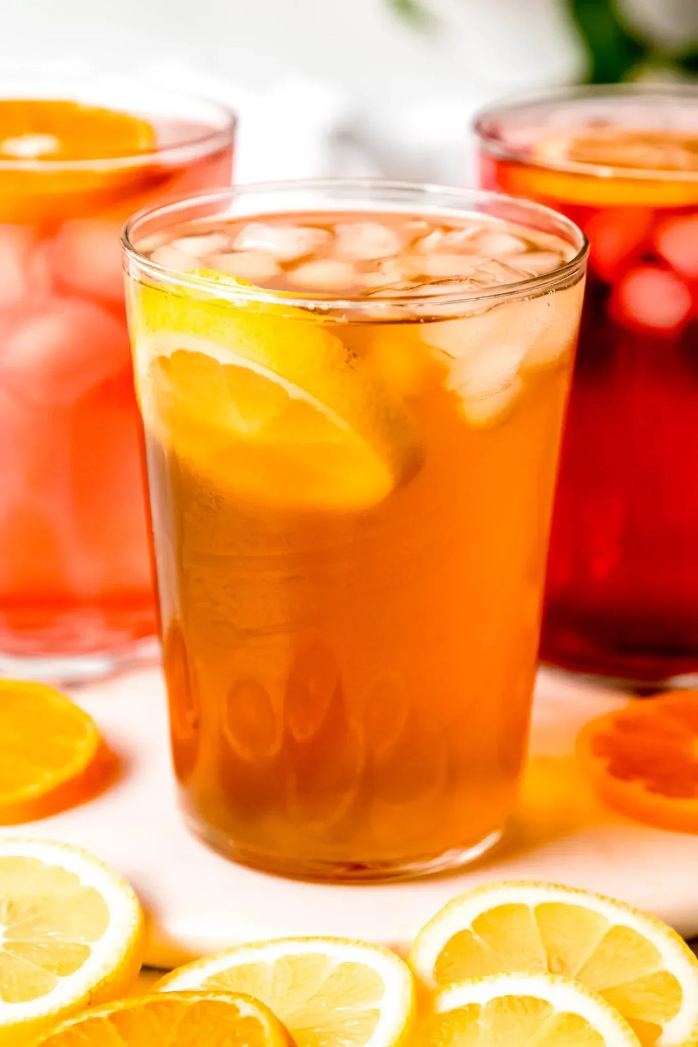 Iced tea with lemon slices in a tall glass surrounded by fresh citrus on a bright white surface, from Yerba Buena Tea Company.