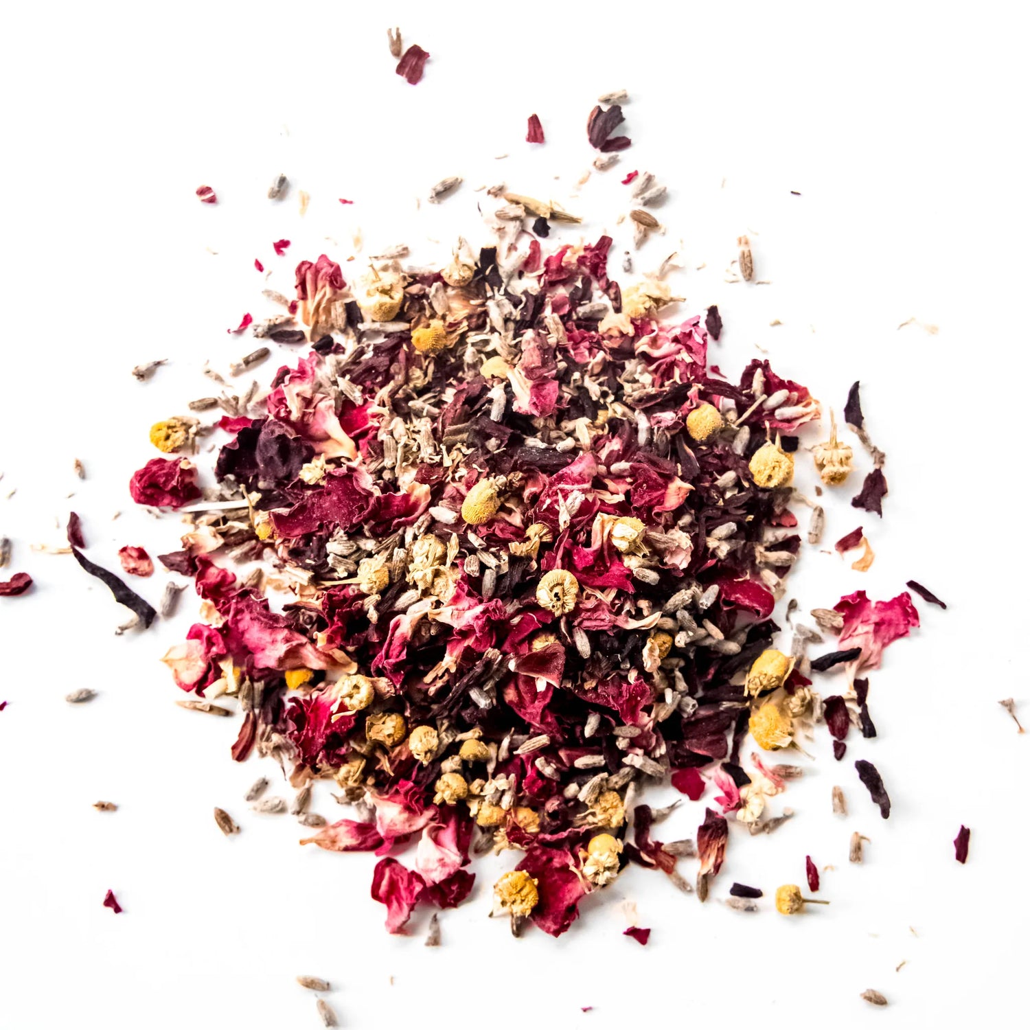 Loose leaf herbal tea blend with red rose petals, chamomile flowers, and dark herbs scattered on white background, by Yerba Buena Tea Company.