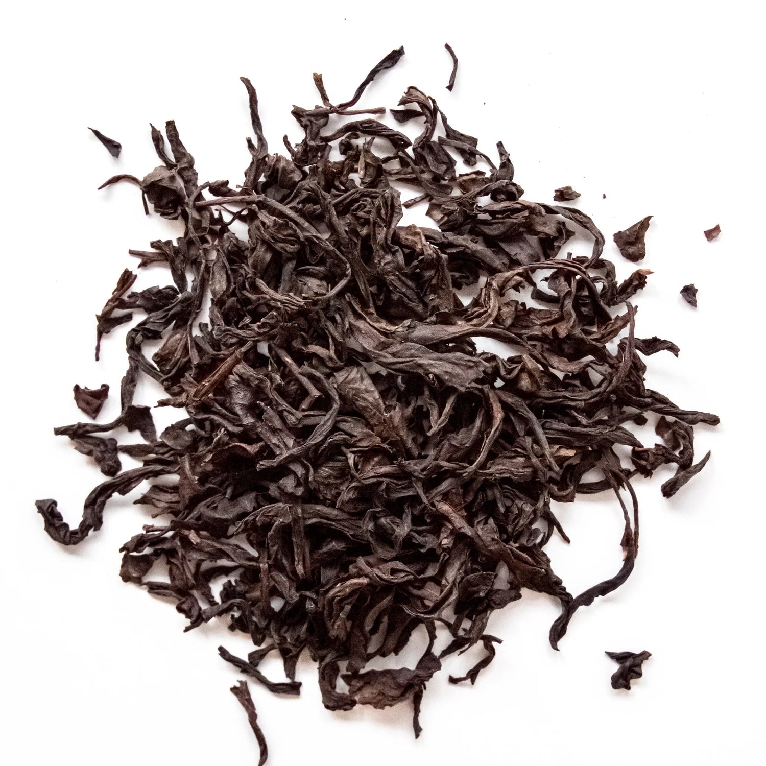 Curled dark brown oolong tea leaves scattered loosely on white background, by Yerba Buena Tea Company.