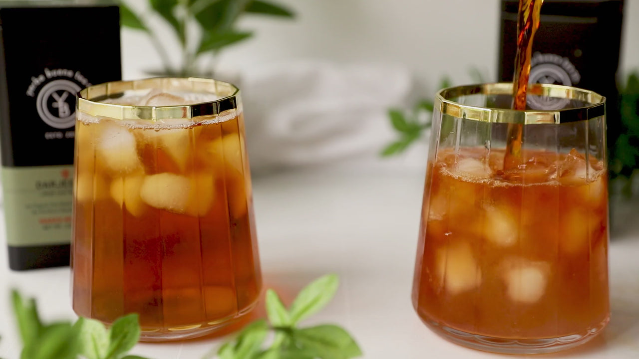 Iced tea poured over ice in two gold-rimmed glasses, with organic loose leaf tea tins and fresh mint