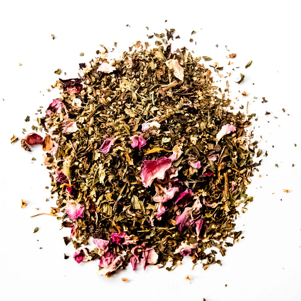 Loose leaf herbal tea blend with dried rose petals scattered on white background, by Yerba Buena Tea Company.